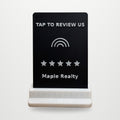 Real photo of the Tap-to-Review counter stand with a sample business name, on a clean studio background (background added digitally)