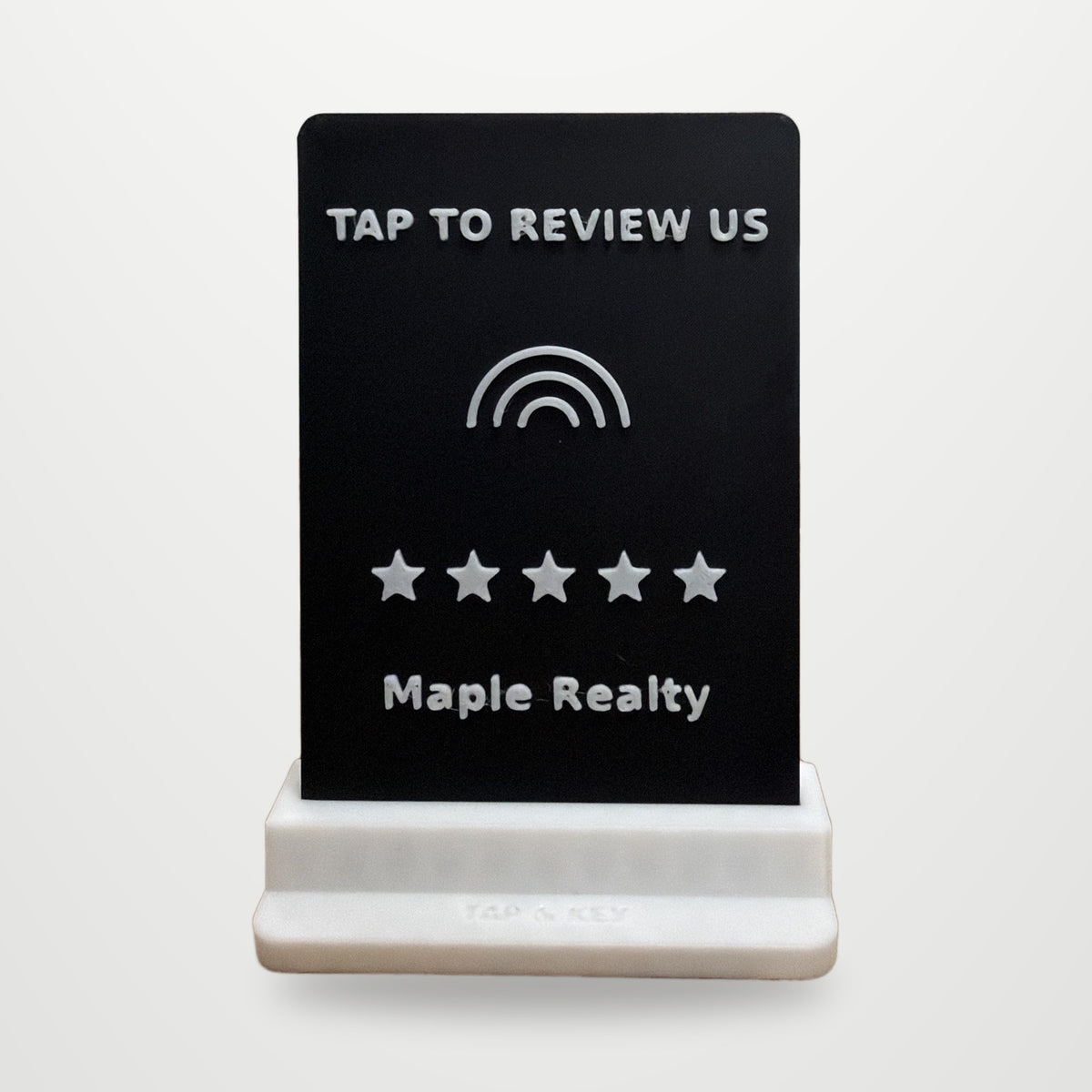 Real photo of the Tap-to-Review counter stand with a sample business name, on a clean studio background (background added digitally)