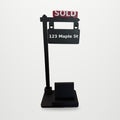 SOLD Sign Phone Stand with red SOLD rider and 123 Maple St sign, on a clean studio background (background added digitally)