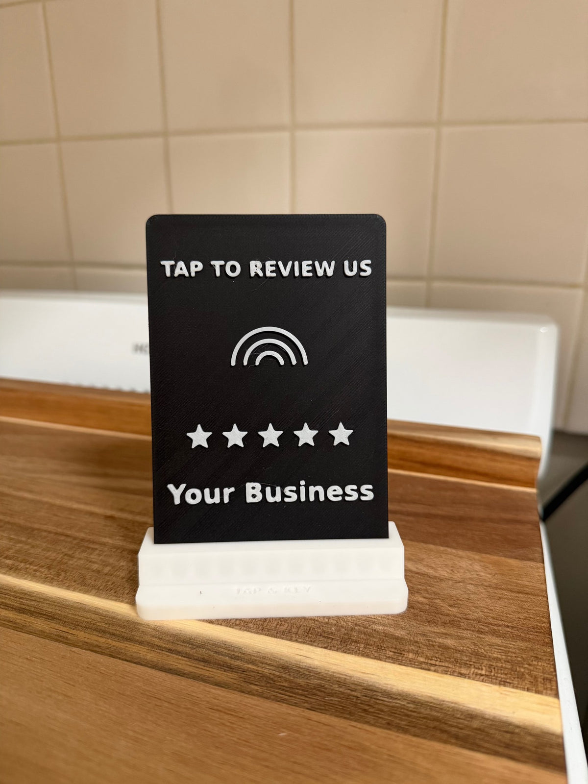 Real photo: Tap to review us counter stand, black plaque with white text and stars in a white Tap & Key base
