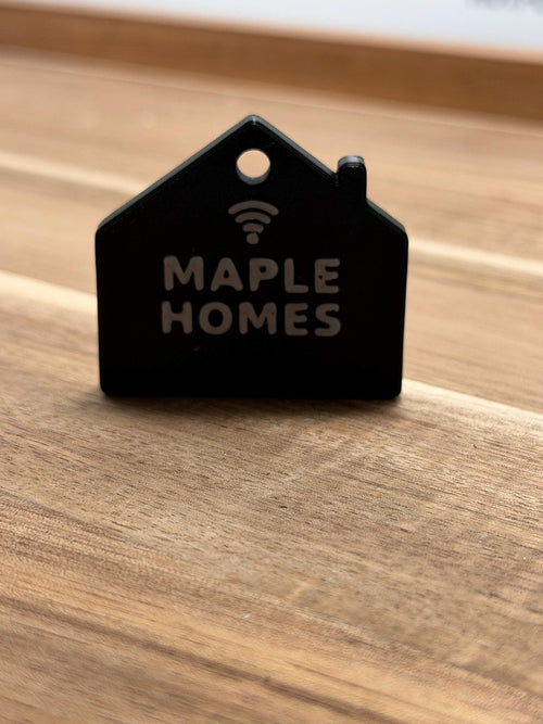 Real printed NFC house keychain, sample text MAPLE HOMES, on a wood table